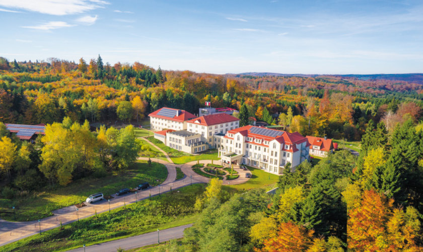Luftaufnahme eines Hotels mit roten Dächern, umgeben von herbstlich gefärbten Wäldern Luftaufnahme eines Hotels mit roten Dächern, umgeben von herbstlich gefärbten Wäldern