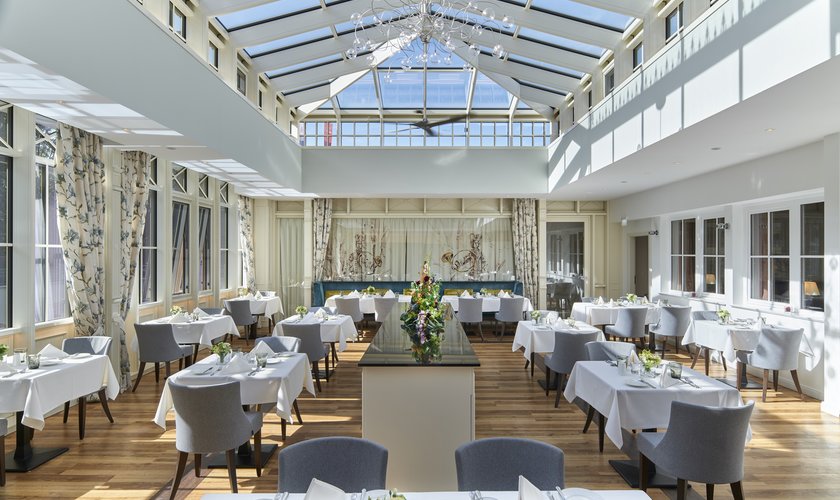 Heller, eleganter Speisesaal mit Glasdach und stilvoll gedeckten Tischen im Tagungshotel im Harz.